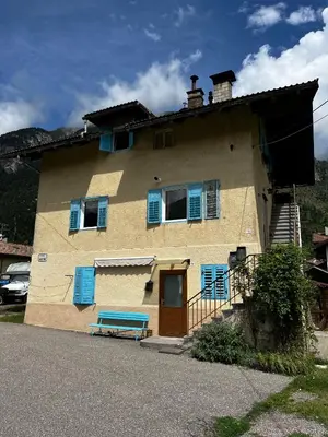 a house with blue shutters and a blue bench in front at Appartamento Le Sipole in Ziano di Fiemme
