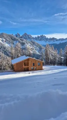a wooden building in the snow with mountains in the background at Munt Dolomiti Farm in Plancios