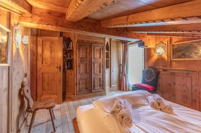 a bedroom with wooden walls and a bed and a chair at Casa Cirmoli, confortevole mansarda con balcone panoramico in Cortina dʼAmpezzo