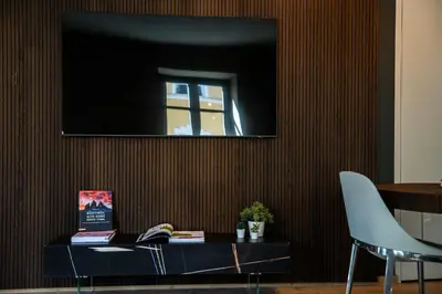 a television on a wall with a table and a chair at KODERLE SUITE K3 Genziana in Brunico