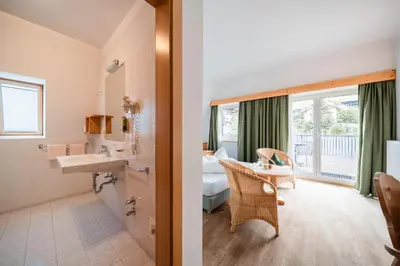 a bathroom with a sink and a bedroom at Hotel Pütia in Antermoia