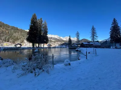 a river with snow on the ground next to a town at Rifugio di Niki in Falcade