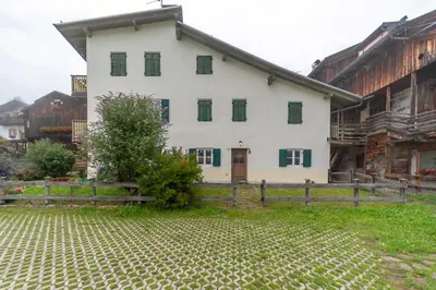 a white house with green windows and a fence at Casa Tamion in Vigo di Fassa