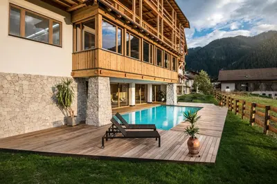 a house with a wooden deck with a swimming pool at Dependance Hotel Mareo Dolomites in San Vigilio Di Marebbe