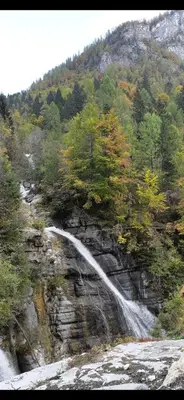 a waterfall on the side of a mountain with trees at Appartamento Sot le Pale in Taibon