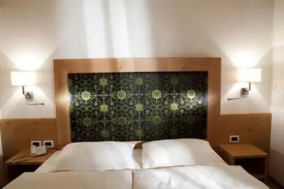a bedroom with a bed and two lamps and a wall at Hotel Christian in Corvara in Badia