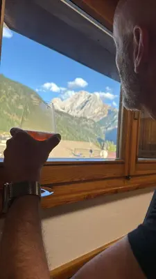 a man holding a glass of wine looking out a window at Appartamento DOLOMITES con BOX privato in Canazei