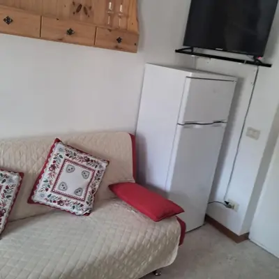 a white couch with a red pillow and a refrigerator at Villa Cecilia mono in Tonadico