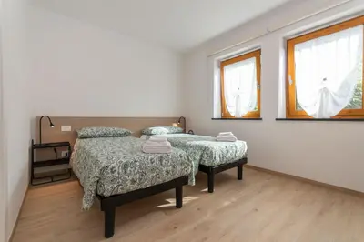 two beds in a room with two windows at Casa Serena in Dolomiti Agordine in Taibon