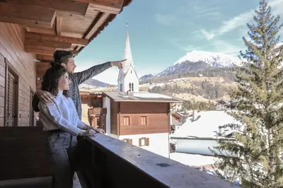 two people standing on a balcony looking at a snow covered mountain at Parc Hotel Posta in San Vigilio Di Marebbe