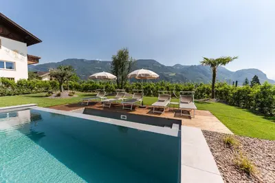 a pool with chairs and umbrellas next to a house at Hotel Garni Sonngart in Andrian