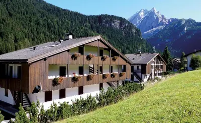 a building on a hill with mountains in the background at Residence Canazei in Alba di Canazei
