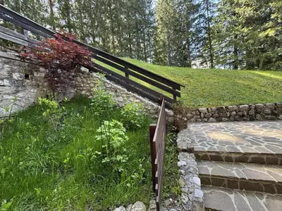 a wooden fence next to a stone wall and stairs at Casa Bucaneve 2, confortevole a due passi dal centro in Cortina dʼAmpezzo