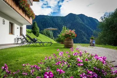 a garden with chairs and an umbrella and flowers at Apartments Raffl in Ortisei