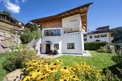 a large white house with a yard with yellow flowers at Apartments Miara in Santa Cristina in Val Gardena