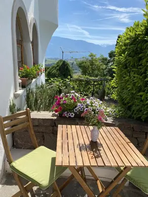 a wooden table and chairs on a patio with flowers at Platzlhof in Appiano sulla Strada del Vino