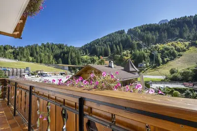 a balcony with pink flowers on a wooden railing at Pivan Apartments in Selva di Val Gardena