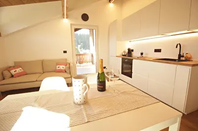 a kitchen and living room with a table with a bottle of wine at Guest House Dezulian in Castello di Fiemme