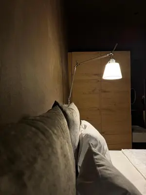 a person sitting on a bed with a lamp at La Maison 35 - Bruneck - zentral gelegene Appartments in Brunico
