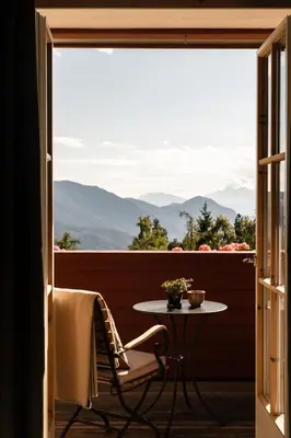 a table and chair on a balcony with a view of mountains at Berghoferin Fine Hotel & Hideaway in Redagno