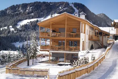 a large wooden house in the snow with a fence at Mayr Natur Apartments in Santa Cristina in Val Gardena