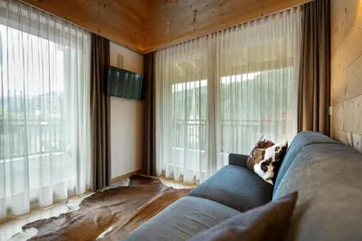 a living room with a blue couch and large windows at Mayr Natur Apartments in Santa Cristina in Val Gardena