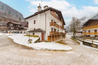 a building with snow on the ground next to a street at Sasso Bianco Home - Mountain View & Private Parking in Sottoguda