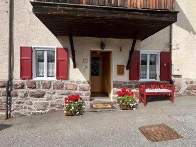 a building with red doors and a bench and flowers at Casa Gabry by Sunhome Fiemme in Varena