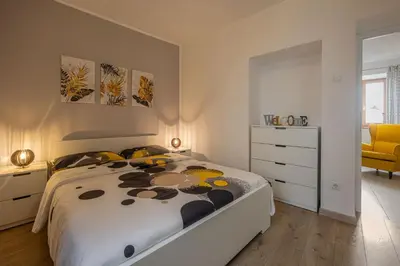 a white bedroom with a bed and a yellow chair at Ferienhaus Karin in Cortaccia