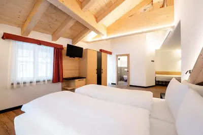 a bedroom with two white beds and a flat screen tv at Albergo Garni Edy (B&B) in Canazei