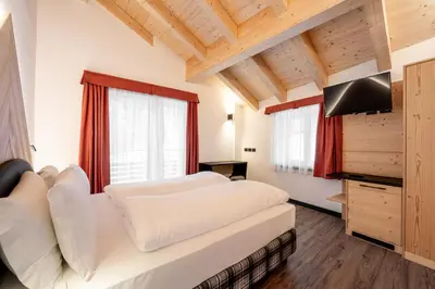 a bedroom with two white beds and red curtains at Albergo Garni Edy (B&B) in Canazei