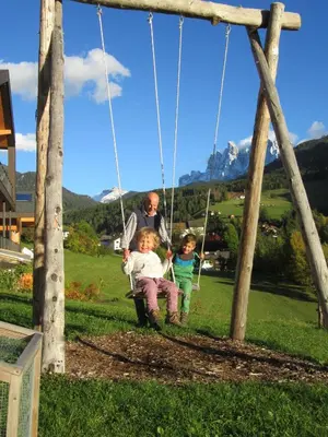 a man and two children sitting on a swing at Peterwieshof in Funes