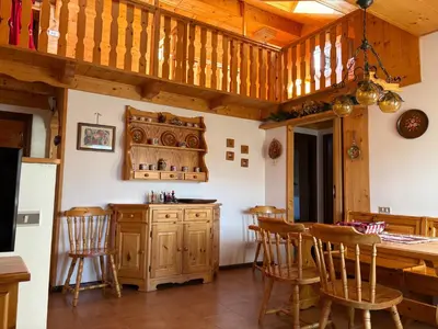 a kitchen with wooden cabinets and a bar with chairs at Mansarda Veronza in Castello di Fiemme