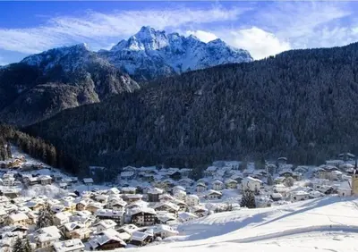 a town in the snow with mountains in the background at Rifugio TEA Dolomiti in Falcade