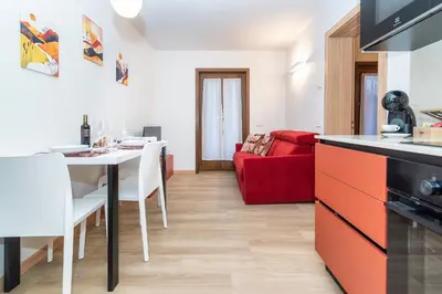 a kitchen and living room with a table and a red couch at Larice&Ribes Apartments in San Vito di Cadore