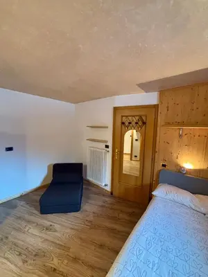 a bedroom with a bed and a blue chair at Pragma Apartments - Dolomiti by Valentina in Moena