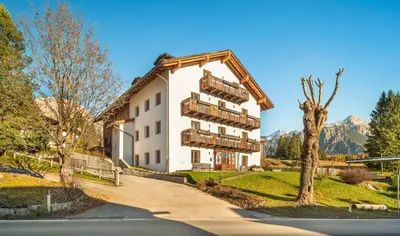 a white building with balconies and a tree at Cademai Alpenglow Chalet with Sauna R&R in Cortina dʼAmpezzo