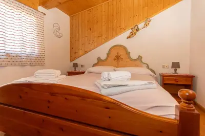 a bedroom with a wooden bed with white sheets at Casa Paola in Rocca Pietore