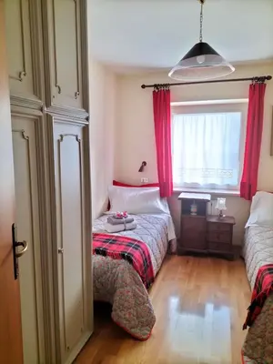 a bedroom with two beds and a window with red curtains at Appartamento l'angelo in Predazzo