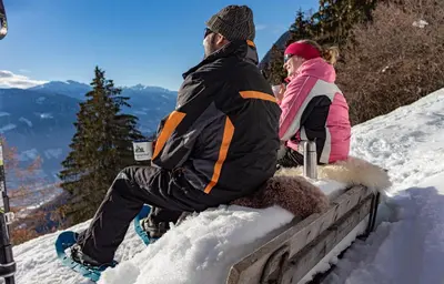 two people sitting on a bench in the snow at Unterthurnerhof in Rifiano