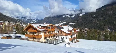 a large wooden house in the snow in the mountains at Casa Davarda - Appartamento Cima Dodici in Vigo di Fassa