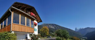 a building with flowers in the window and mountains at Prantschurhof in San Pietro in Gardena