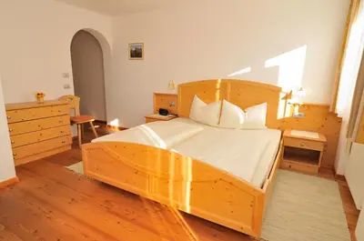 a bedroom with a large wooden bed with white sheets at Prantschurhof in San Pietro in Gardena