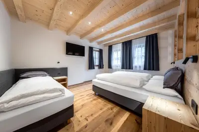 two beds in a room with wooden floors and windows at Ciasa Francësch in La Villa
