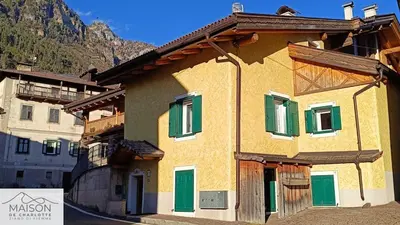 a house with green shuttered windows and a mountain at La Maison de Charlotte - Val di Fiemme in Ziano di Fiemme