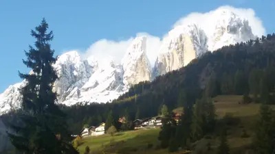 a snow covered mountain range with a house in a field at Appartamento Ivo in Campitello di Fassa
