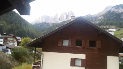 a brown and white building with mountains in the background at Appartamento Ivo in Campitello di Fassa