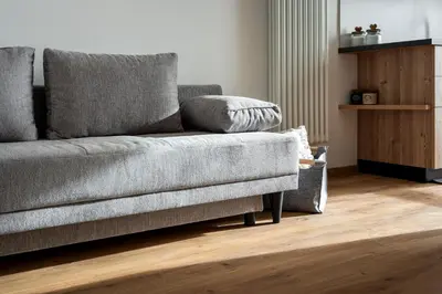 a grey couch in a living room with a wooden floor at Happiness 14 in Castello di Fiemme