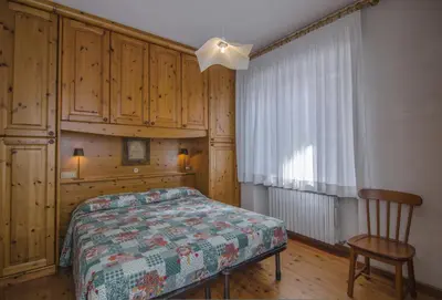 a bedroom with a bed and a chair and a window at La tua coccola a Cortina in Cortina dʼAmpezzo