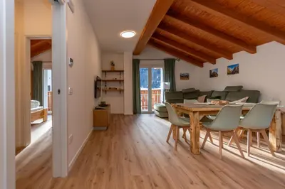 a dining room and living room with a wooden table and chairs at Hapina Dolomiti with Garage in Cencenighe